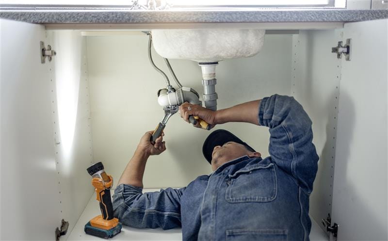 Plumber repairing pipes beneath a bathroom sink in Santa Monica